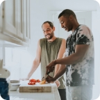 Two young men cook dinner together in kitchen. 